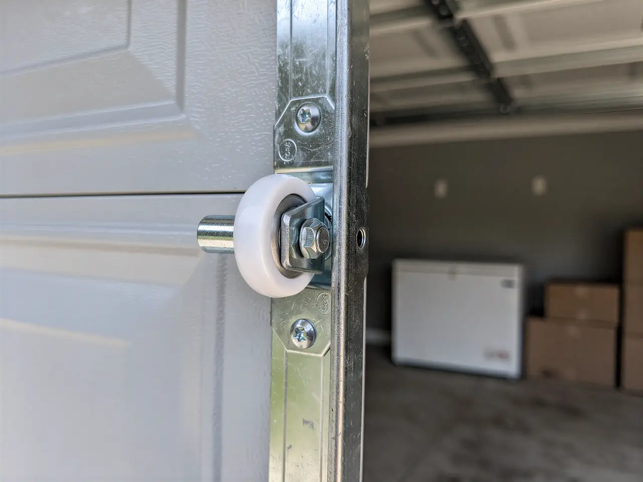 A white garage door roller is attached to a metal track.